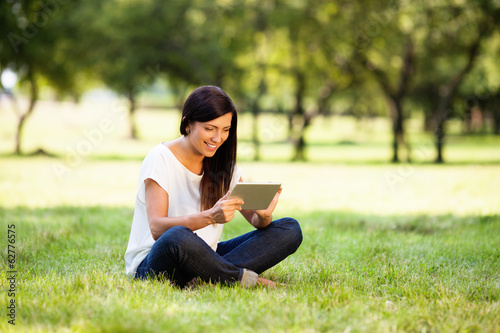 Happy young woman with digital tablet sitting on grass in park © baranq