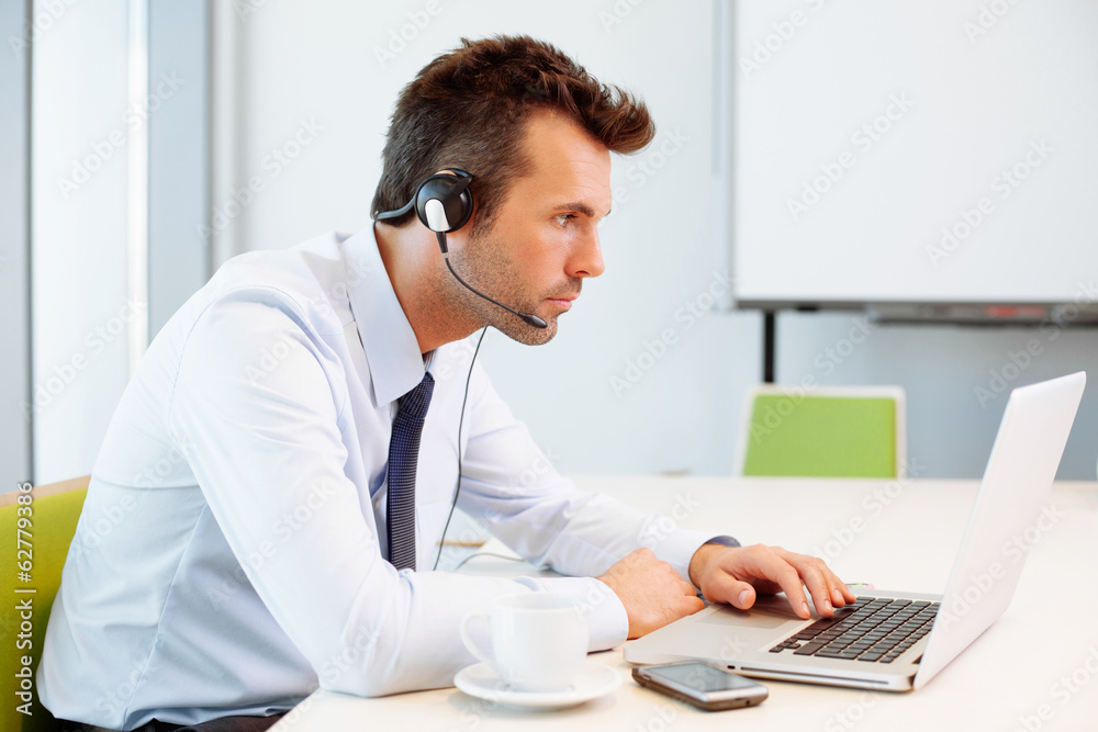Busy man working on laptop with headset Busy man working on laptop with headset