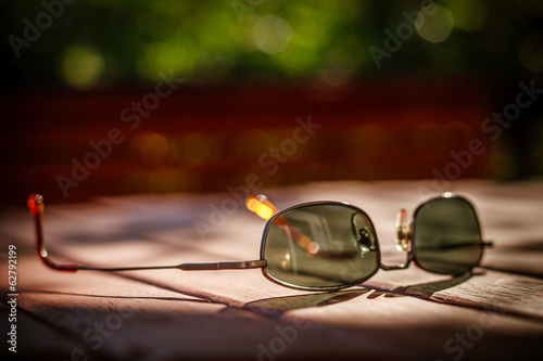 Used sunglasses on wooden table in spot of sunlight. photo