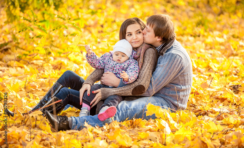 Young family sitting on leaves at autumn park Young family sitting on leaves at autumn park