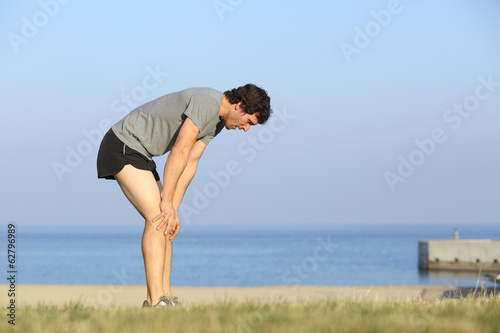 Exhausted runner man resting on the beach after workout