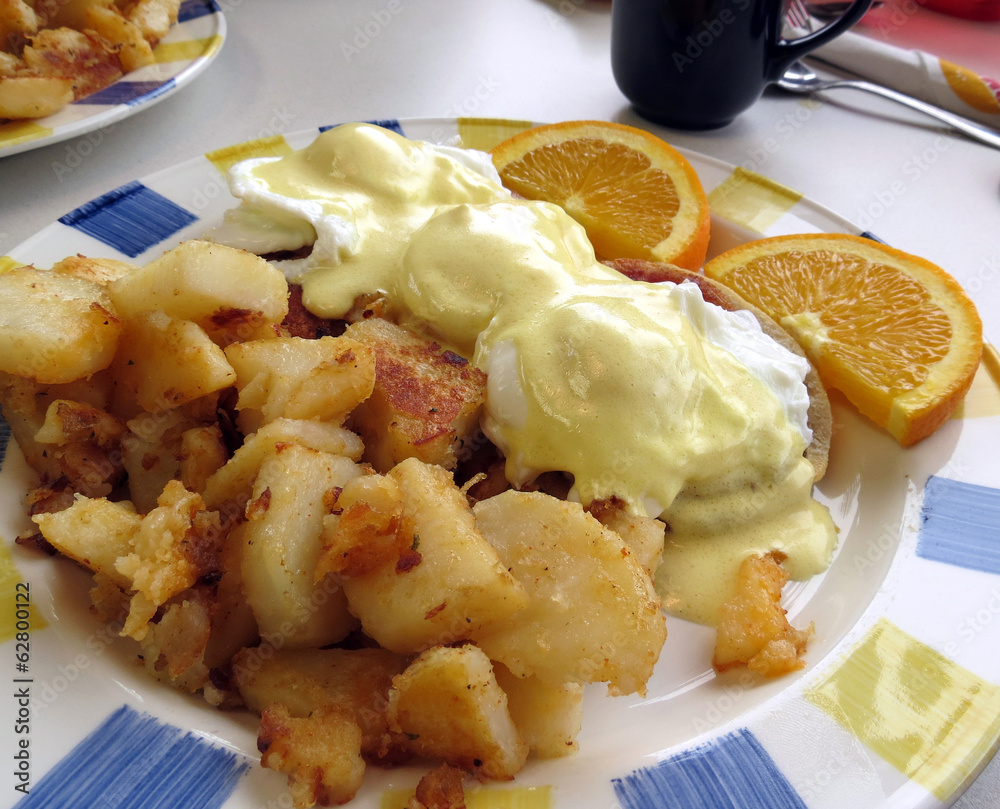 Eggs Benedict served with homefries and garnished with orange slices.