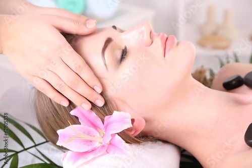Beautiful young woman having head and stone massage in spa