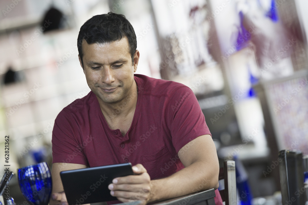 A cafe interior. A man sitting using a digital tablet. A cafe interior. A man sitting using a digital tablet.