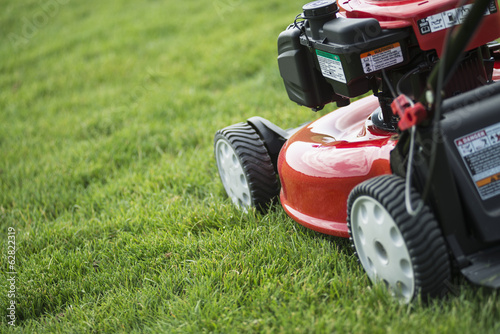 A young man mowing the grass on a property, tending the garden, using a petrol lawnmower.  photo