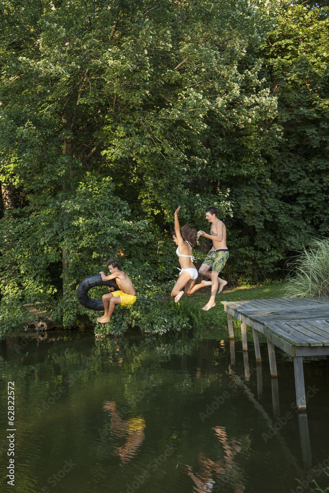 Three young boys jumping from the jetty into a still pool of water. Three young boys jumping from the jetty into a still pool of water.
