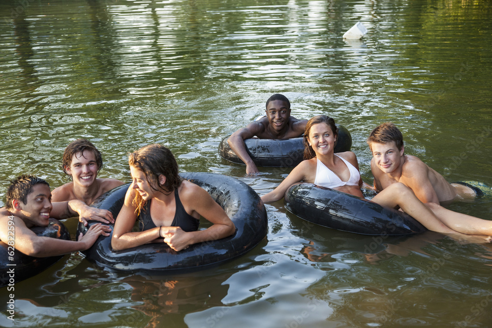 A group of young people, boys and girls, swimming and floating using swim floats and inflated tyres. 
