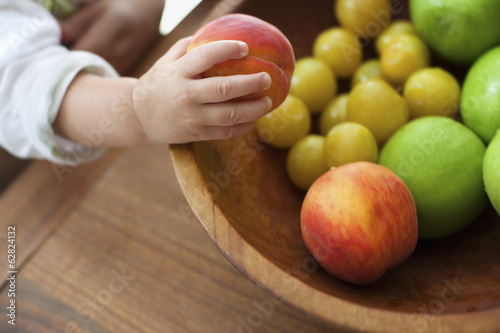 Baby girl's hand grasping peach from wooden bowl
