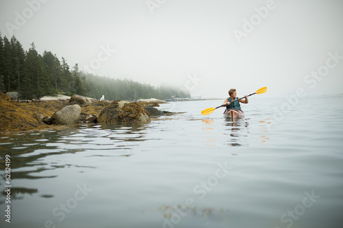 A man paddling a kayak on calm water in misty conditions. New York State, USA