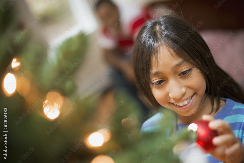 A girl placing a handmade ornament on a Christmas tree. 