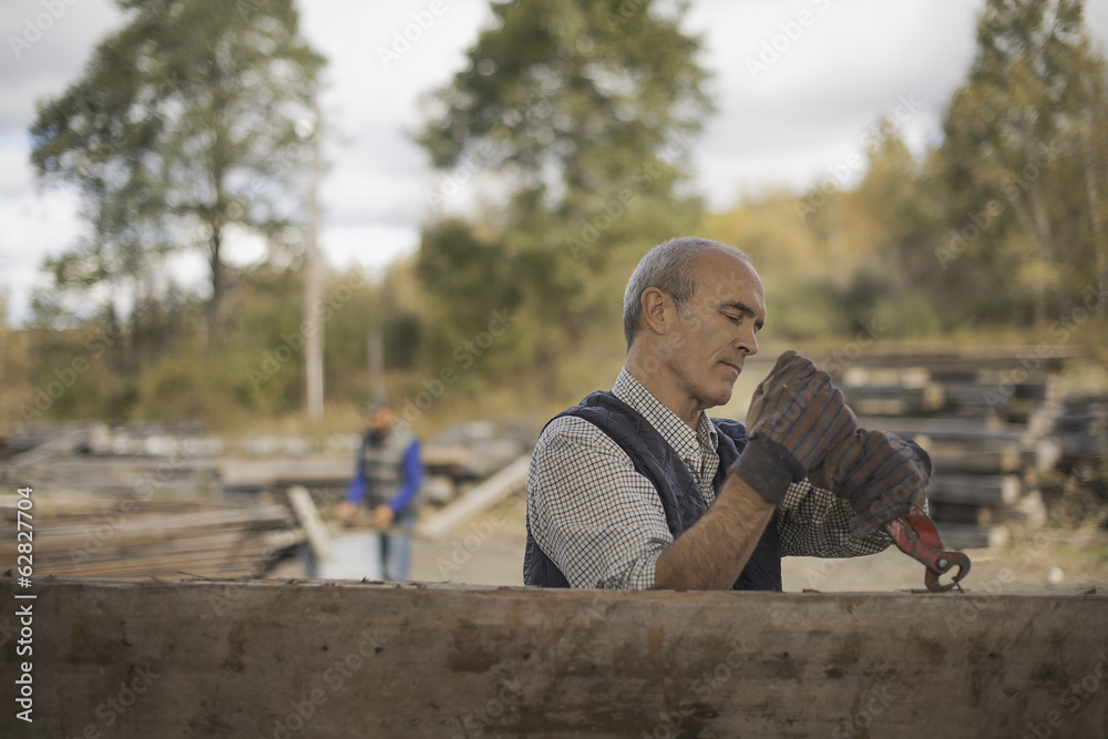 Two men working in a reclaimed timber yard. One using a tool to remove metals from a reclaimed piece of timber. Two men working in a reclaimed timber yard. One using a tool to remove metals from a reclaimed piece of timber.
