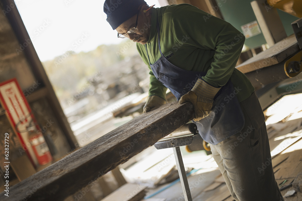 A man examining a large plank of cut wood, in a reclaimed timber yard. A workshop. A man examining a large plank of cut wood, in a reclaimed timber yard. A workshop.