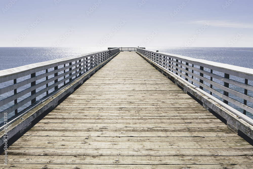 A long pier with railings extending out over the Pacific Ocean leading to the horizon. A long pier with railings extending out over the Pacific Ocean leading to the horizon.