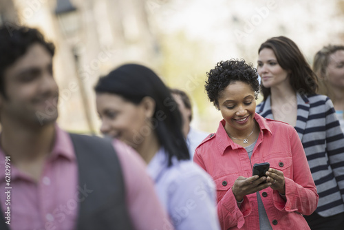 People outdoors in the city in spring time. A woman standing among a group checking her cell phone.
