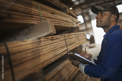 A heap of recycled reclaimed timber planks of wood. Environmentally responsible reclamation in a timber yard. A man with a clipboard by a rack of planks. 