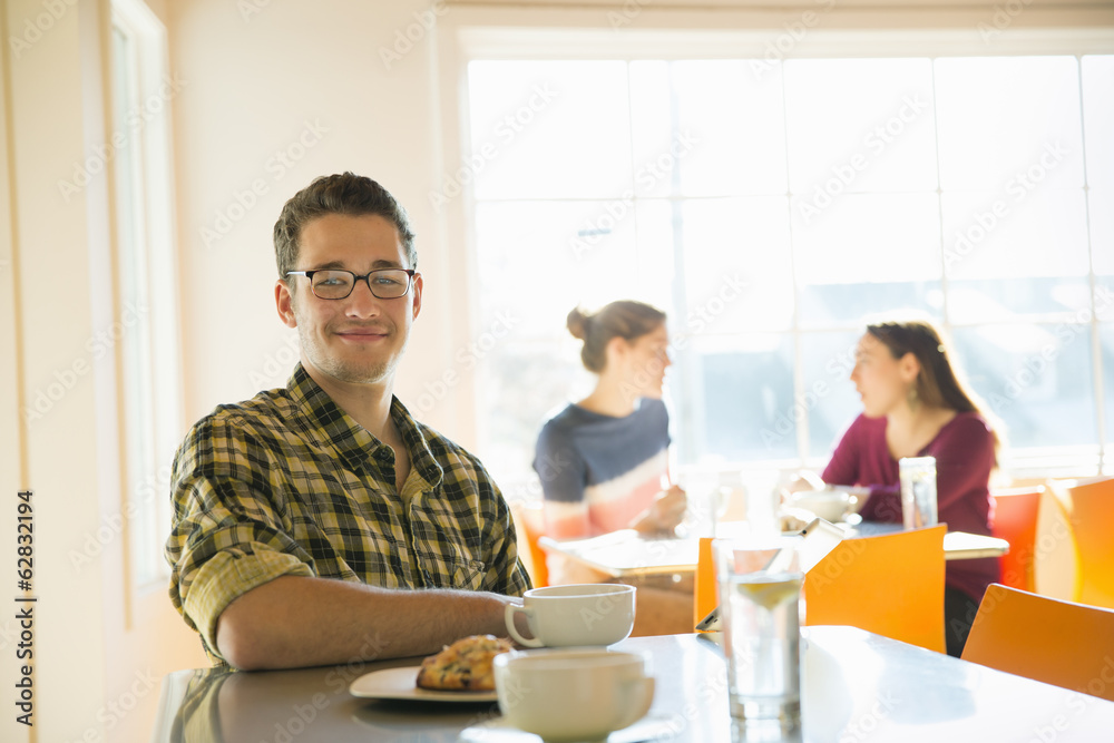 A young man sitting at a coffee shop counter, with two women in the background. A young man sitting at a coffee shop counter, with two women in the background.