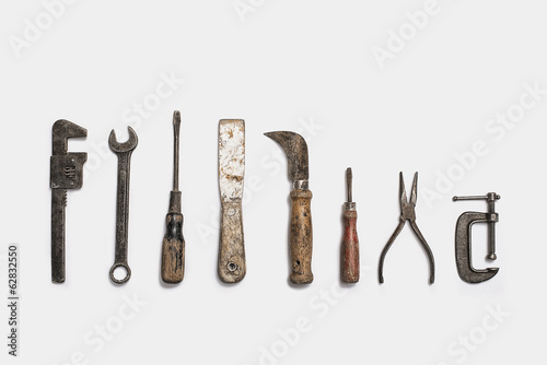 Used tools arranged in a row. Well used, worn handles, shaped wooden smooth texture. Metal rusty and marked implements. 
