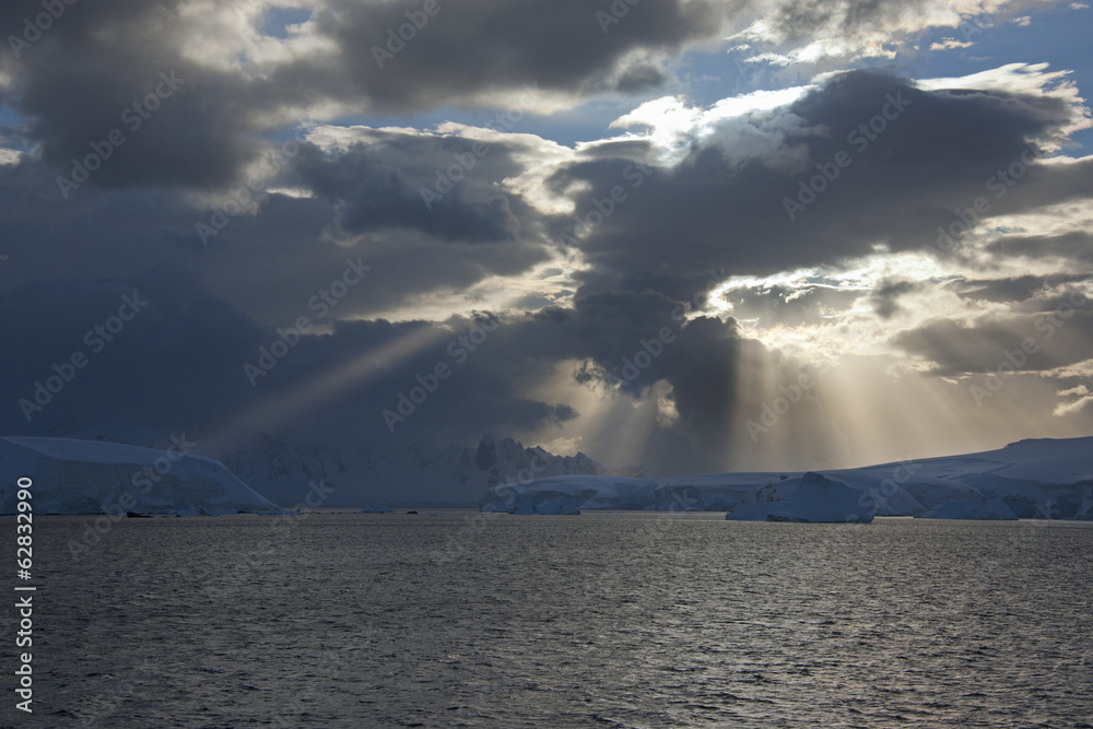 Sun breaking through the storm clouds hitting the icebergs along the west coast of the Antarctic Peninsula. Sun breaking through the storm clouds hitting the icebergs along the west coast of the Antarctic Peninsula.