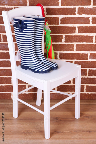 Pair of colorful gumboots on chair on color wall background