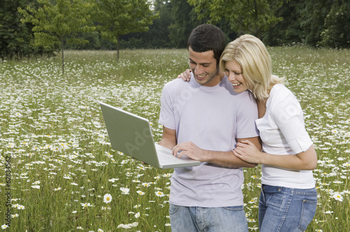 A man and woman in a flower meadow, looking at a laptop screen. photo