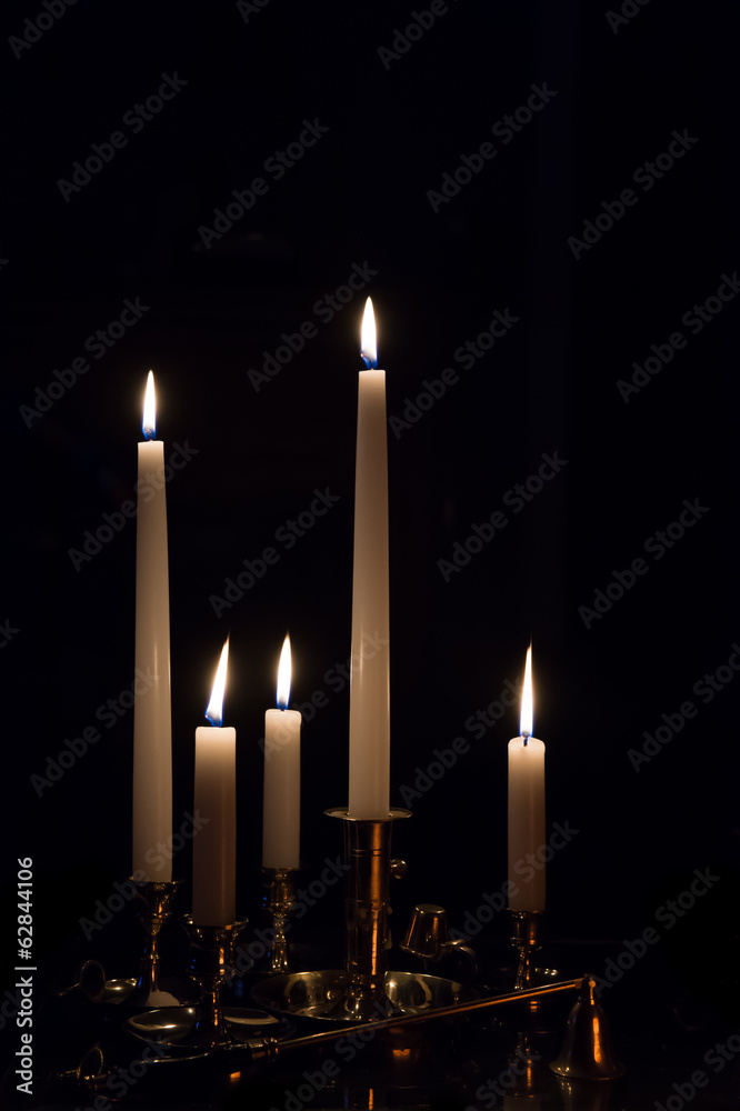 Multiple white burning candles in brass holders Multiple white burning candles in brass holders