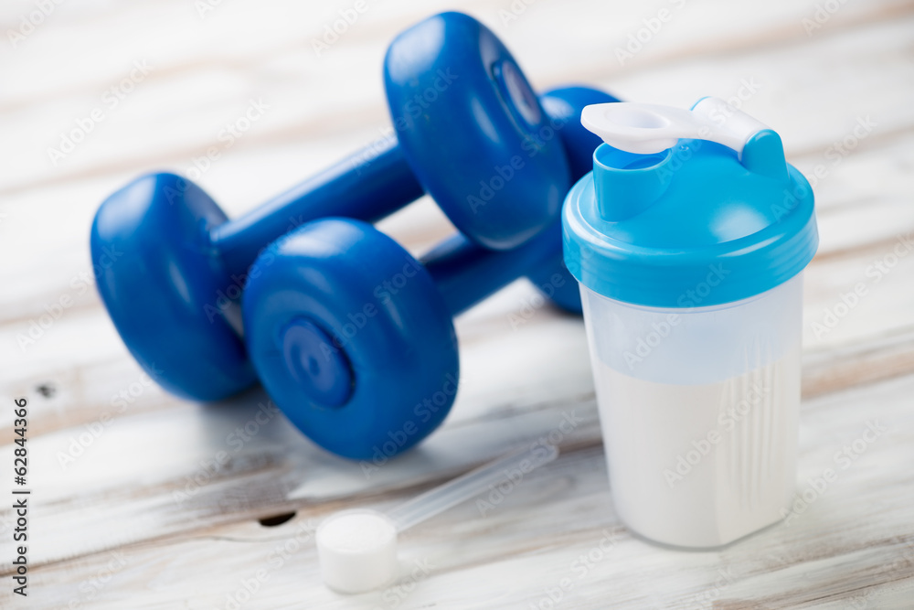 Protein shake and plastic dumbbells on a wooden surface Protein shake and plastic dumbbells on a wooden surface