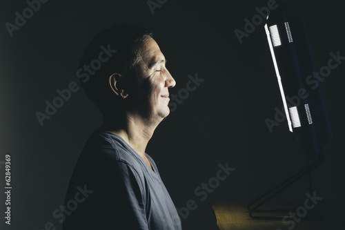 Smiling middle aged man sitting in front of a light therapy box, a full spectrum light box which mimics the sun, and treats people suffering from seasonal affective disorder.