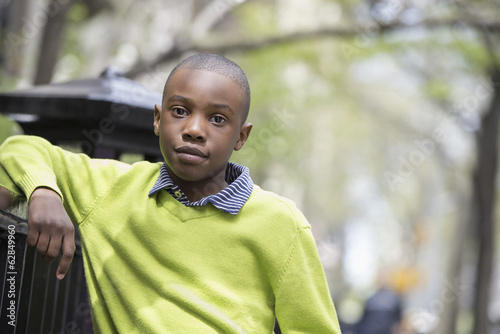 Boy in a green shirt leaning on fence in park