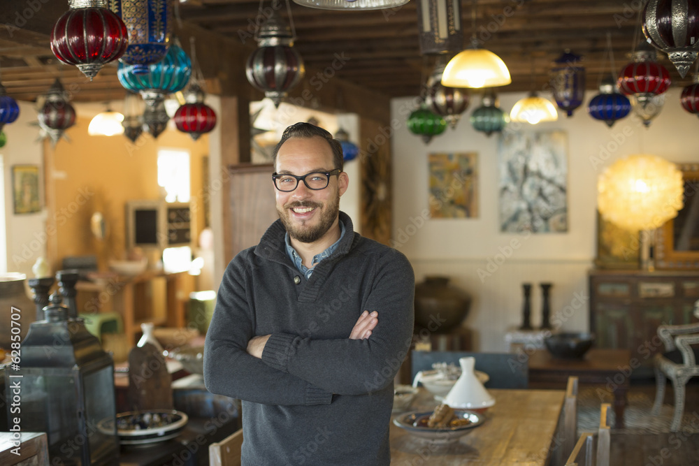 A man standing in a shop full of antique and decorative objects. Antique shop displays. Lighting, glass shades and furniture. A man standing in a shop full of antique and decorative objects. Antique shop displays. Lighting, glass shades and furniture.