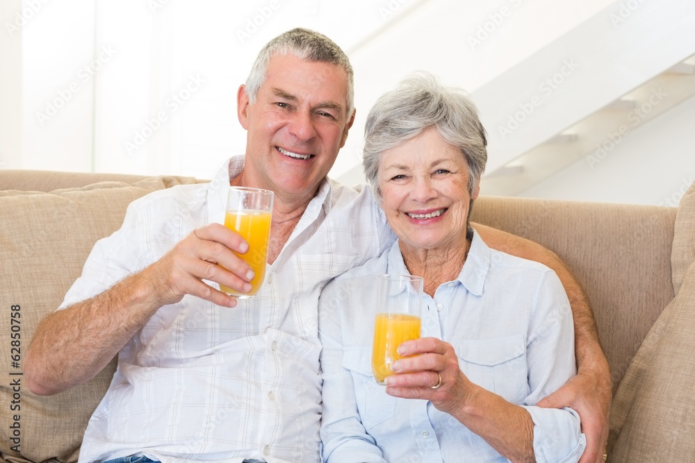Senior couple sitting on couch drinking orange juice