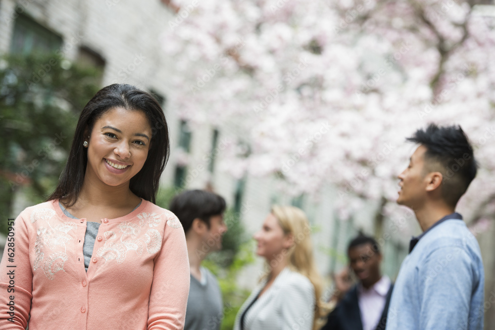 City life in spring. Young people outdoors in a city park. A woman in a pink shirt with four people in the background.