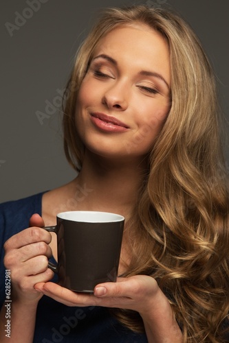 Positive young woman with long hair and blue eyes holding cup