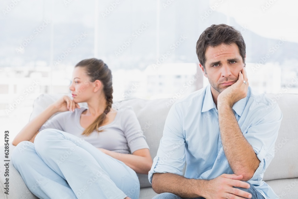Man looking at camera with upset girlfriend on the couch Man looking at camera with upset girlfriend on the couch