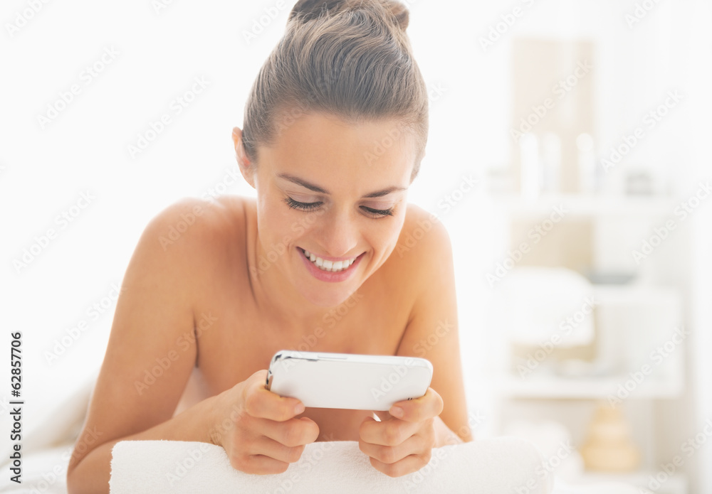 Smiling young woman laying on massage table and writing sms Smiling young woman laying on massage table and writing sms