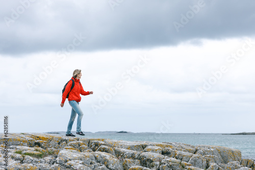 Woman hiker walking on rock against sea background