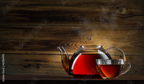 glass teapot with black tea on wooden background