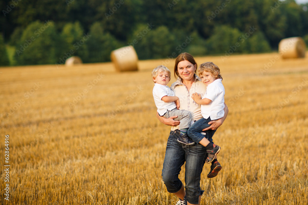 Young mother and two little twins boys having fun on yellow hay Young mother and two little twins boys having fun on yellow hay