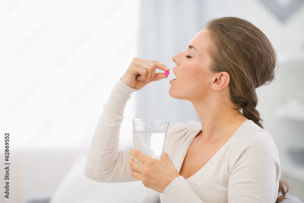 Happy young woman sitting on sofa and taking pill Happy young woman sitting on sofa and taking pill