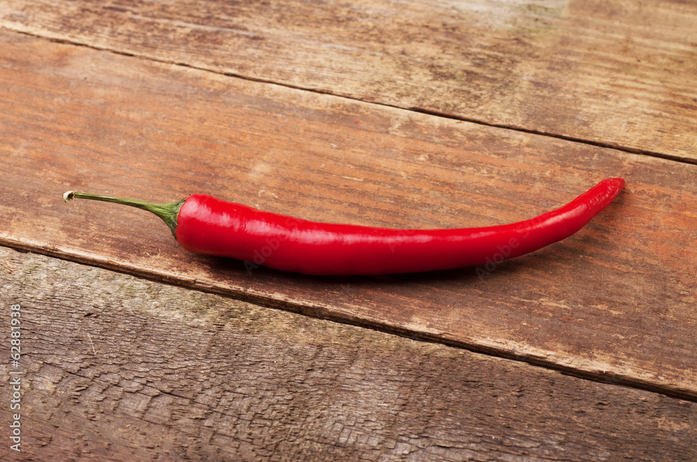 A red chili pepper on a wooden plank A red chili pepper on a wooden plank