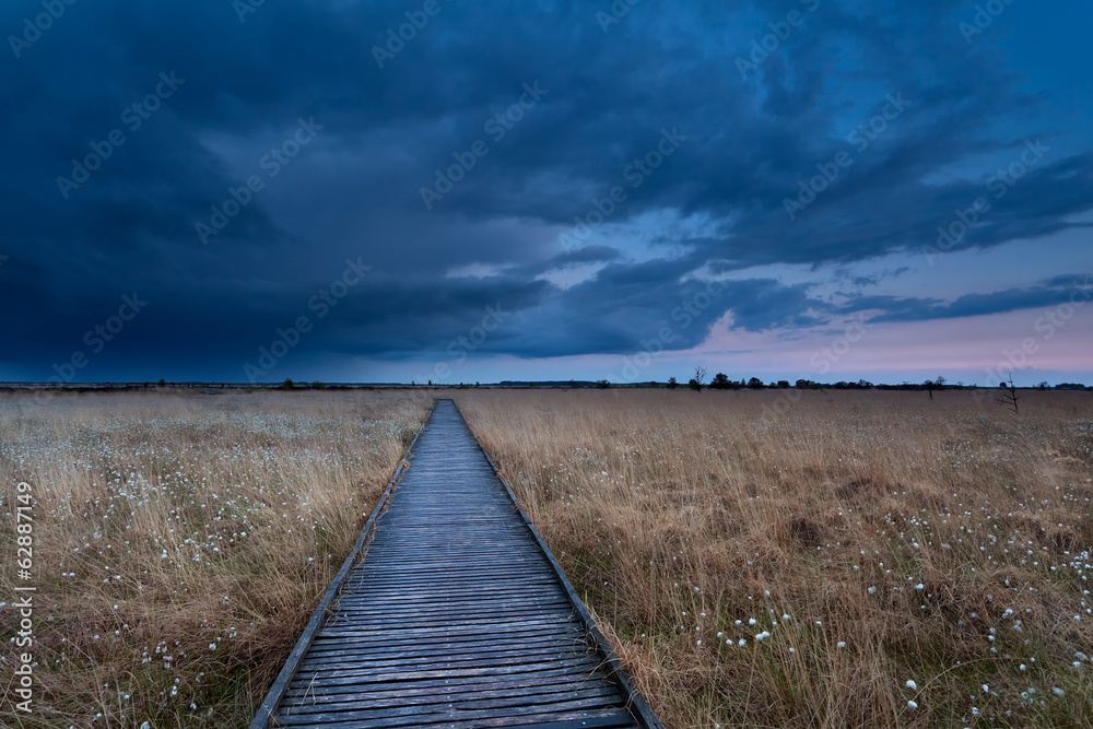 wooden path on marsh at storm during sunset