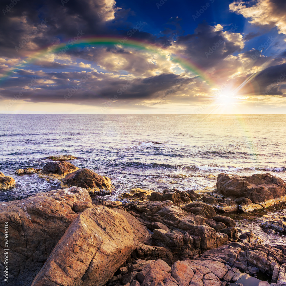 sea wave breaks about boulders at sunset with rainbow