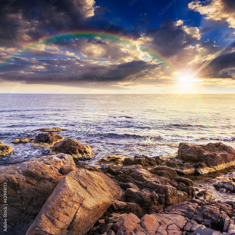 Obraz premium sea wave breaks about boulders at sunset with rainbow