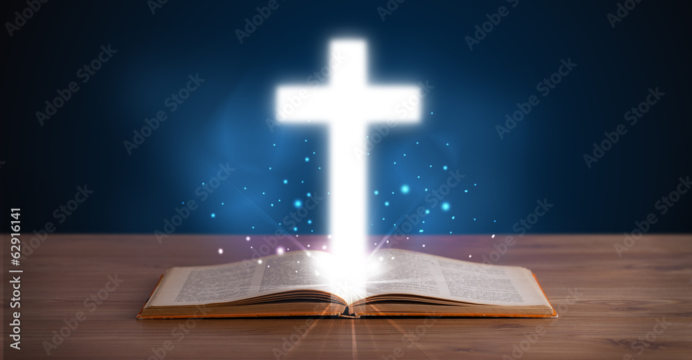 Open holy bible with glowing cross in the middle
