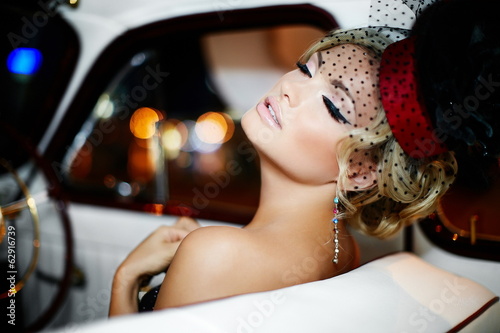 fashion stylish blond girl in retro style sitting in old car