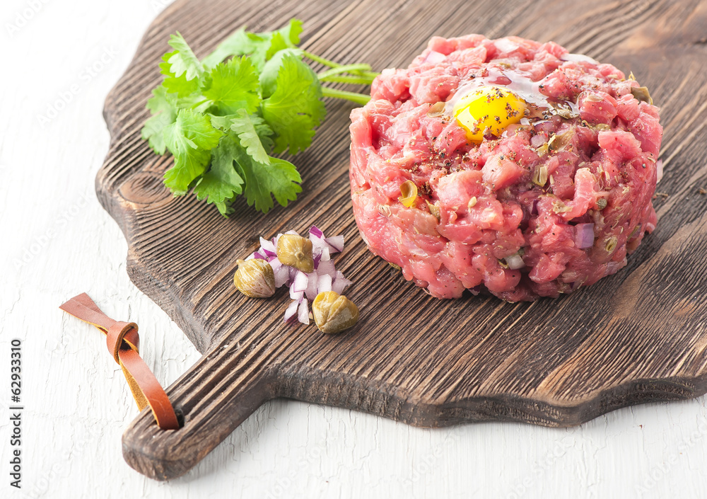 Beef tartare with spices, onions and capers on cutting board