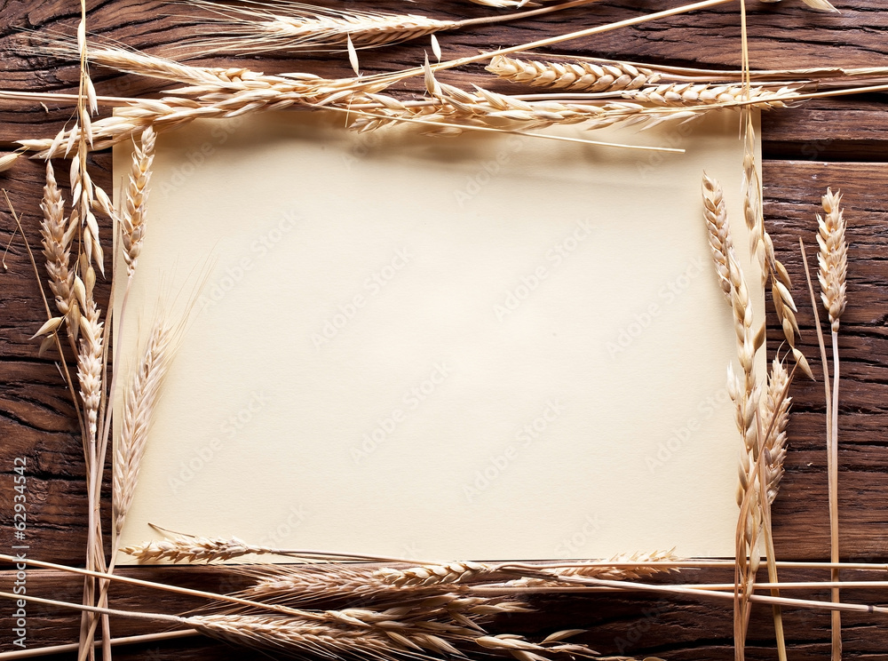 Obraz premium Ears of wheat in the form frame on old wooden table.