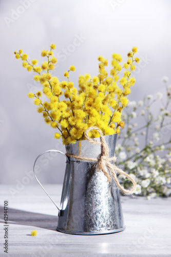Twigs of mimosa flowers in vase on wooden table