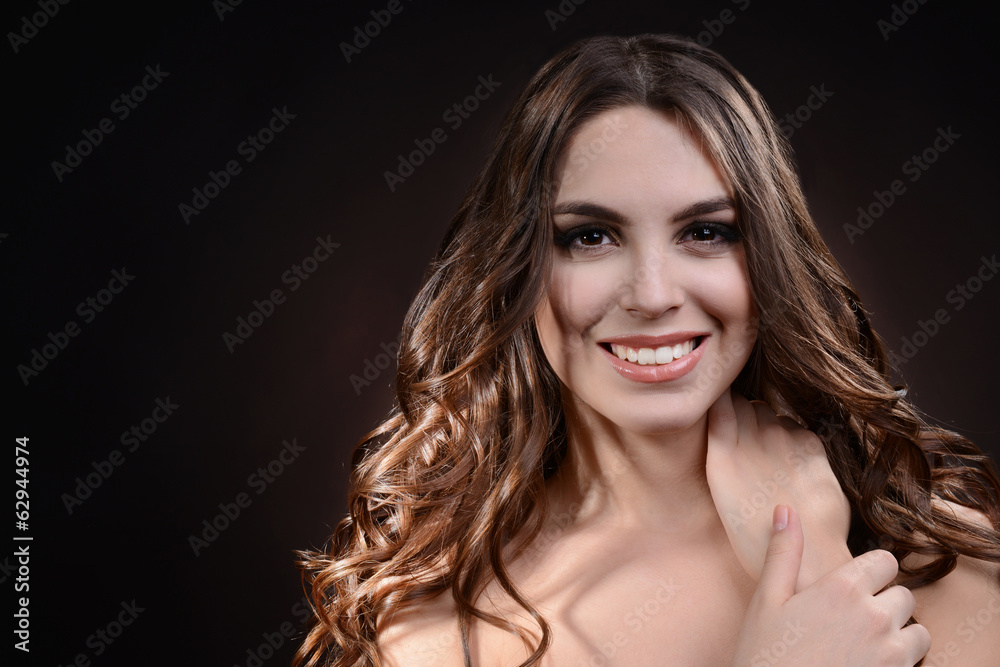 Fototapeta premium Beautiful young woman with long hair on dark brown background