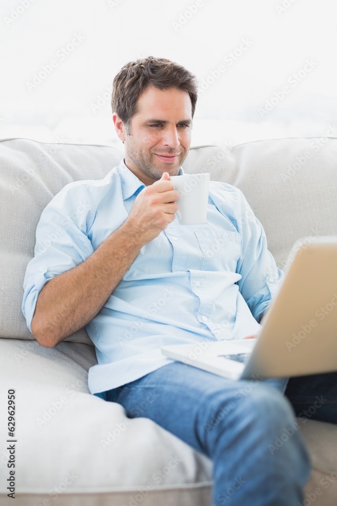 Content man using laptop sitting on sofa having a coffee Content man using laptop sitting on sofa having a coffee