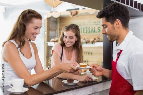 Barista giving pastry to woman at counter in coffee shop